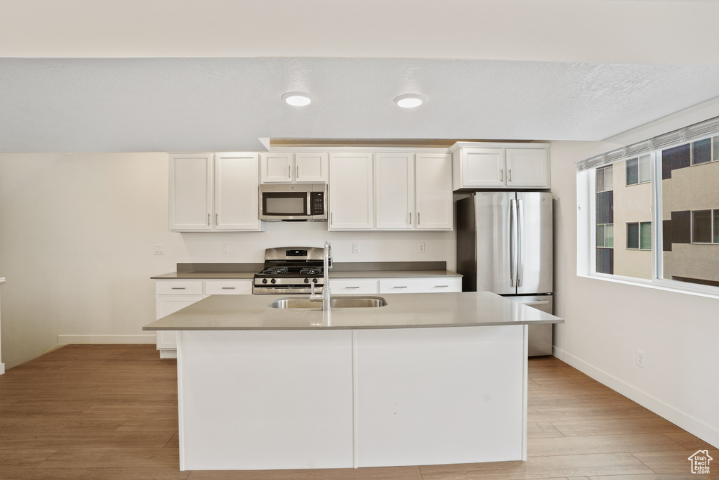 Kitchen with white cabinetry, appliances with stainless steel finishes, light hardwood / wood-style flooring, and a kitchen island with sink