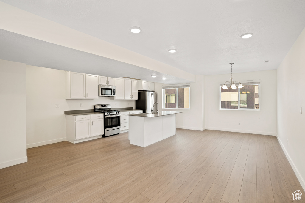 Kitchen with appliances with stainless steel finishes, light hardwood / wood-style flooring, an inviting chandelier, white cabinets, and pendant lighting