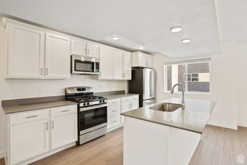 Kitchen featuring appliances with stainless steel finishes, white cabinetry, sink, and an island with sink