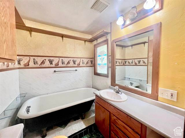 Bathroom with vanity with extensive cabinet space, tile floors, and a tub