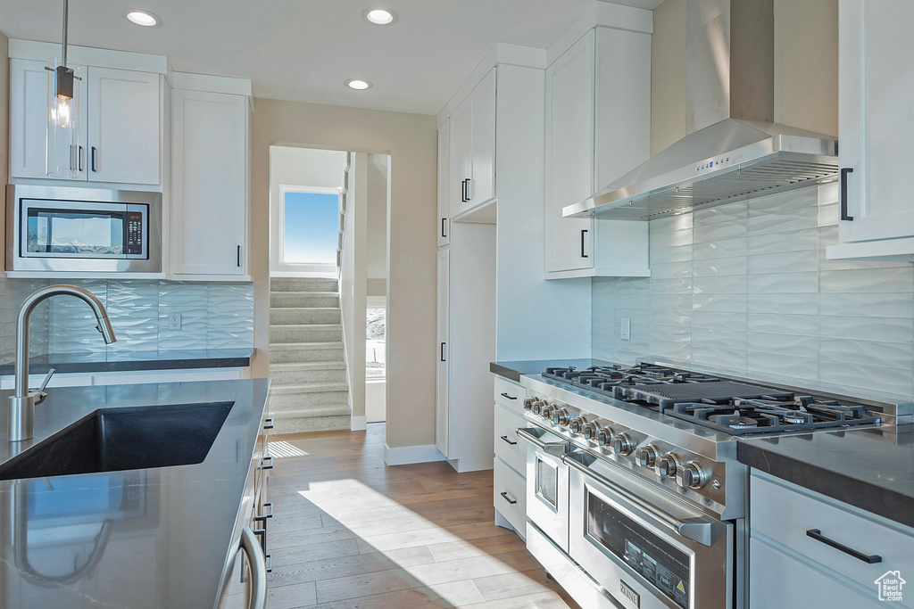 Kitchen with backsplash, wall chimney range hood, stainless steel appliances, light hardwood / wood-style floors, and white cabinetry