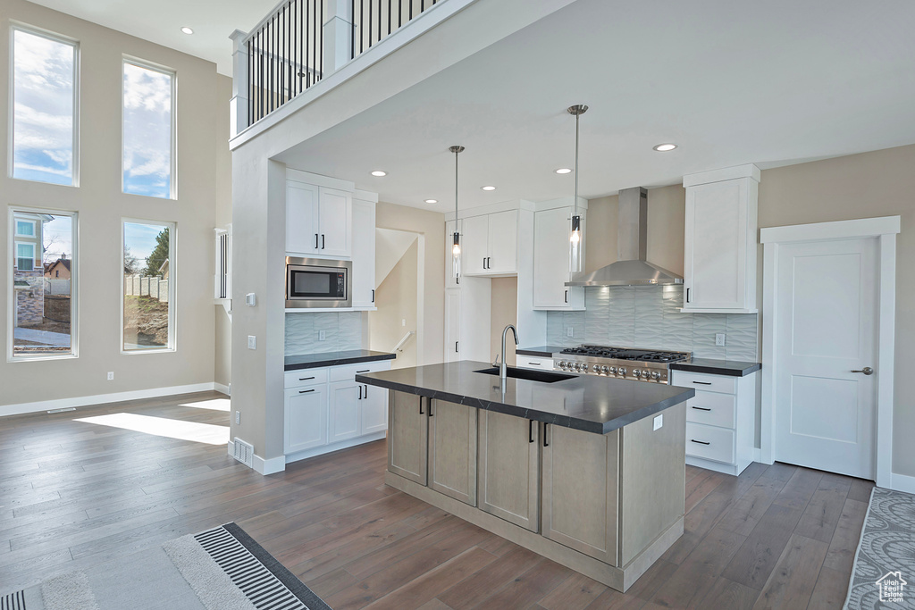 Kitchen featuring backsplash, white cabinetry, stainless steel microwave, and wall chimney exhaust hood