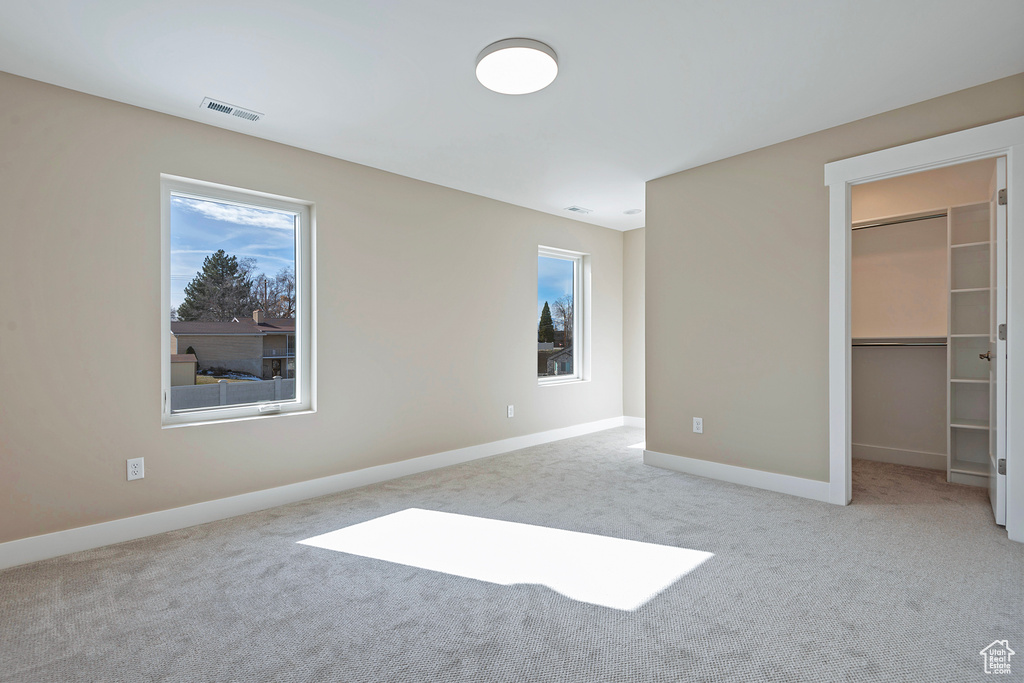 Unfurnished bedroom featuring light colored carpet, a walk in closet, a closet, and multiple windows