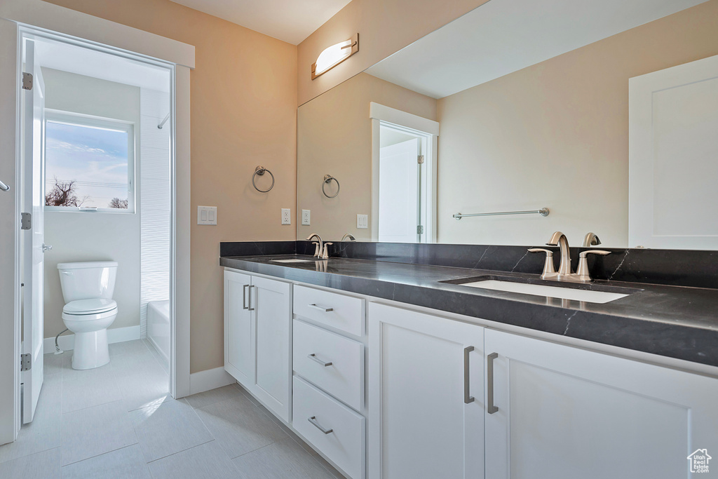 Bathroom featuring dual bowl vanity, tile floors, and toilet