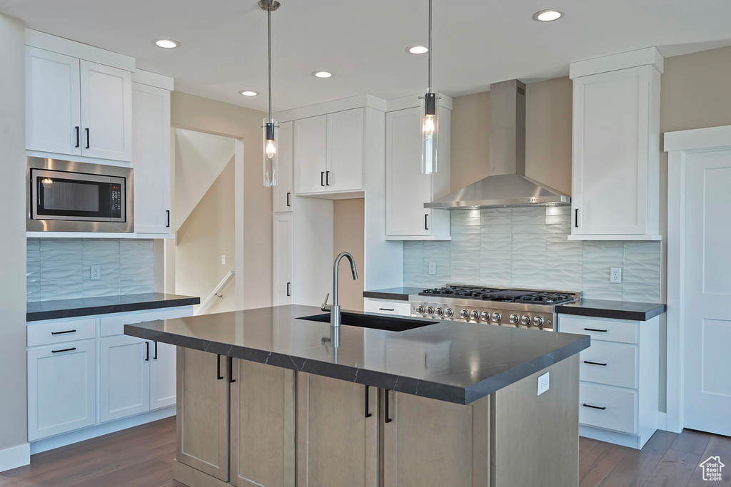 Kitchen featuring pendant lighting, wall chimney range hood, stainless steel microwave, and white cabinets