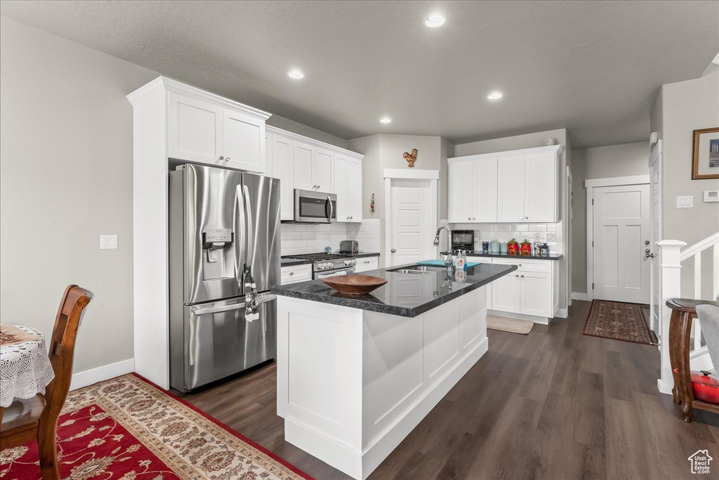 Kitchen featuring dark wood-type flooring, stainless steel appliances, a center island with sink, and backsplash