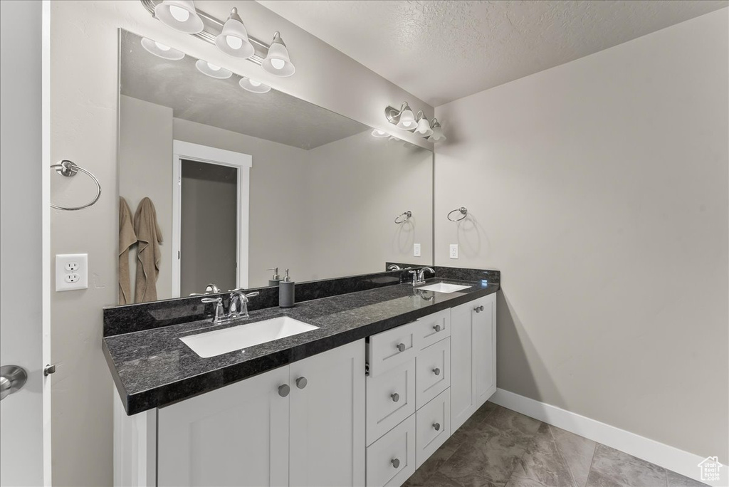 Bathroom featuring a textured ceiling, dual sinks, vanity with extensive cabinet space, and tile floors
