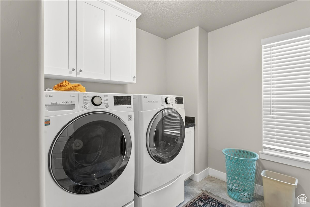 Clothes washing area with a textured ceiling, cabinets, and washer and clothes dryer