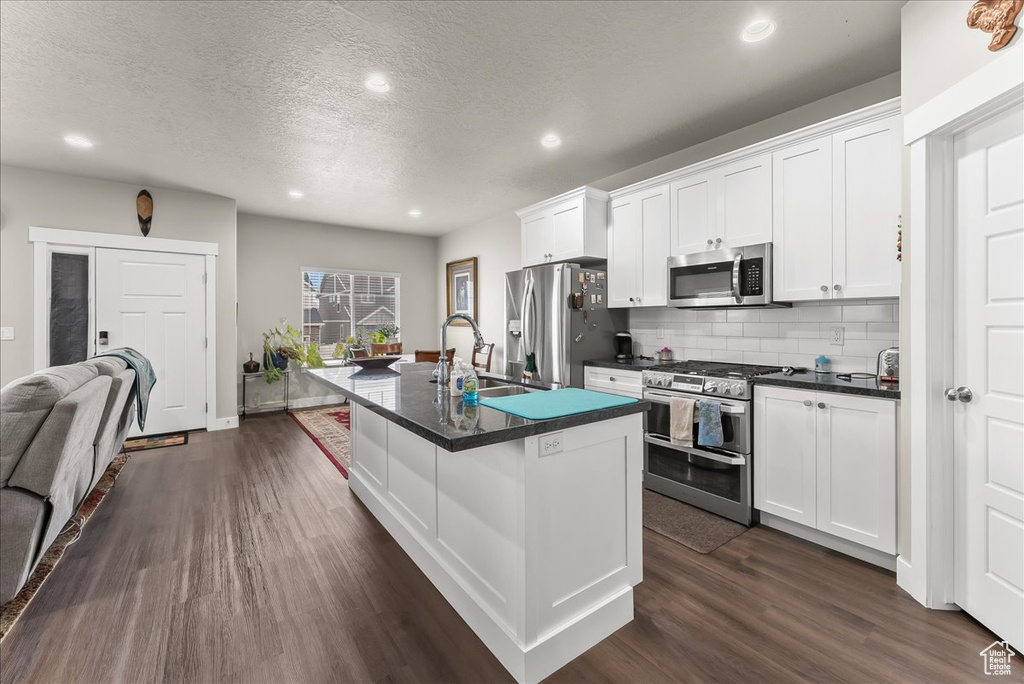 Kitchen featuring a textured ceiling, appliances with stainless steel finishes, dark hardwood / wood-style floors, white cabinetry, and an island with sink