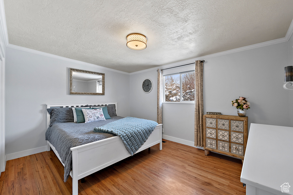 Bedroom featuring light hardwood / wood-style flooring, a textured ceiling, and crown molding