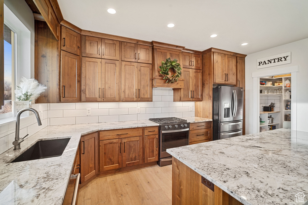 Kitchen with range with gas stovetop, sink, tasteful backsplash, light hardwood / wood-style floors, and stainless steel fridge
