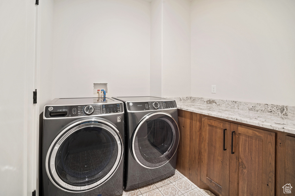 Clothes washing area featuring light tile flooring, washer and dryer, cabinets, and hookup for a washing machine