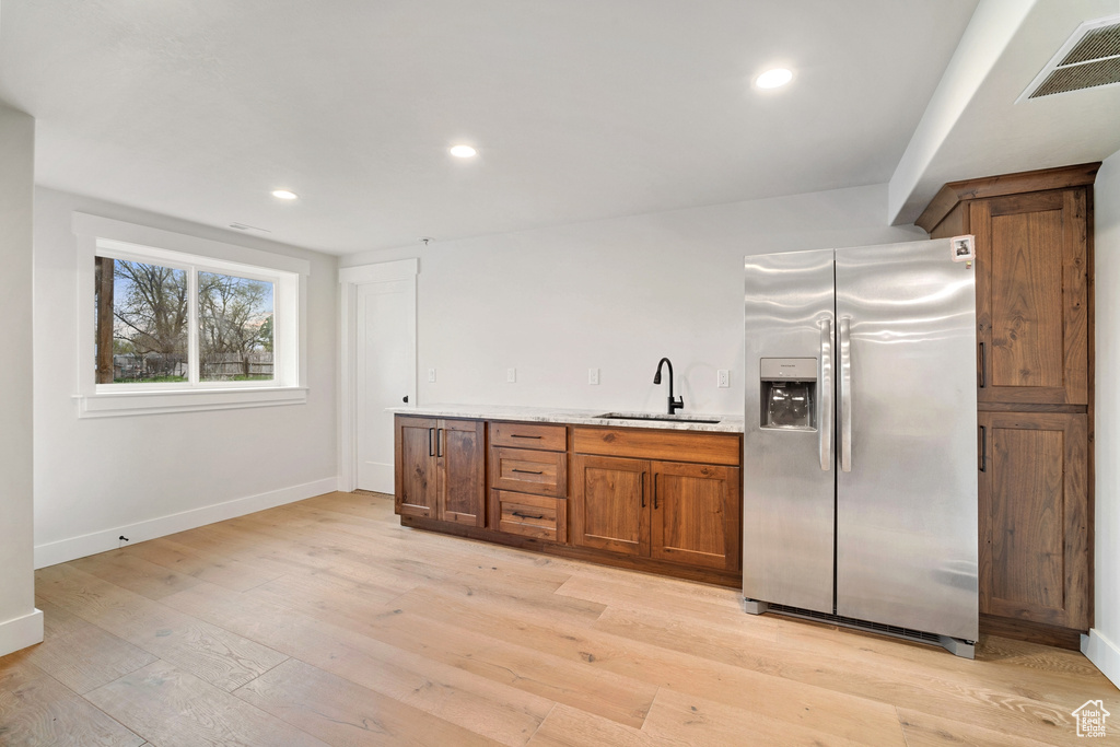 Kitchen with sink, light hardwood / wood-style floors, stainless steel fridge, and light stone counters