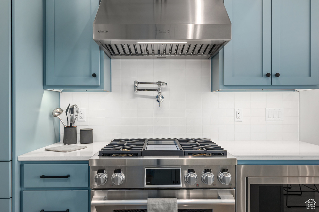 Kitchen featuring blue cabinetry, exhaust hood, stainless steel appliances, and backsplash