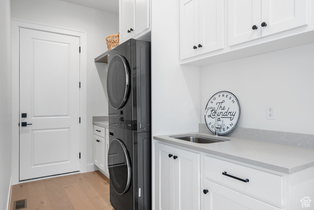 Clothes washing area featuring cabinets, light hardwood / wood-style floors, and stacked washer and clothes dryer