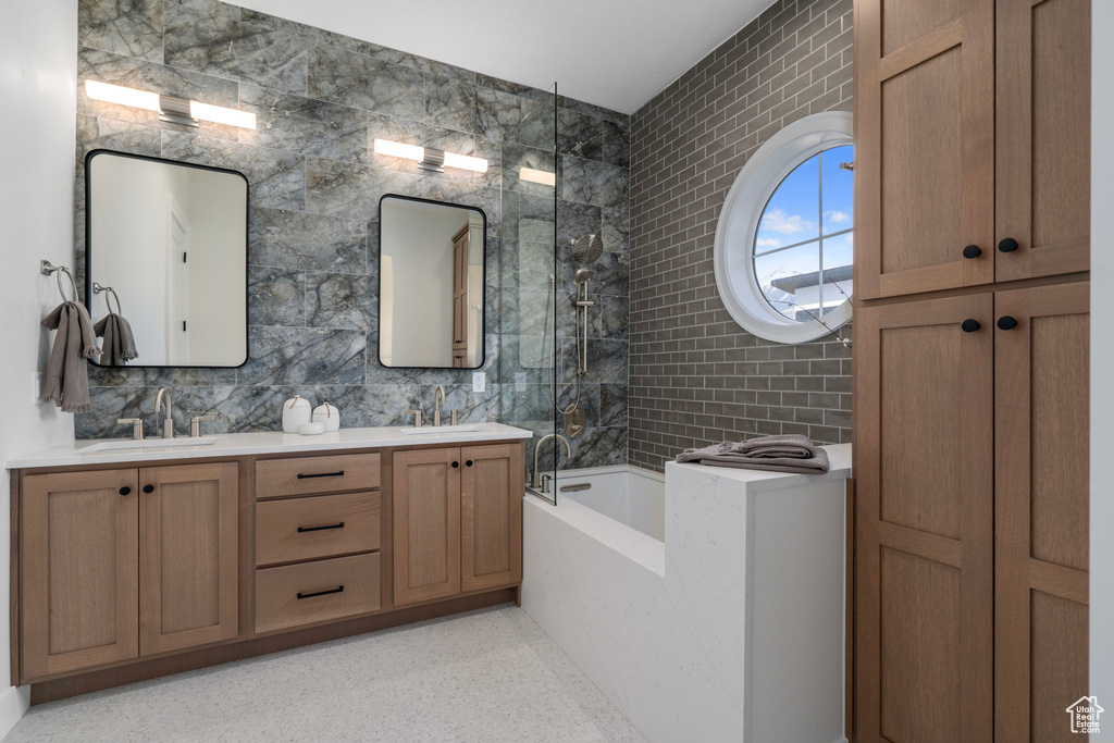 Bathroom featuring a tub, double sink vanity, and tile walls