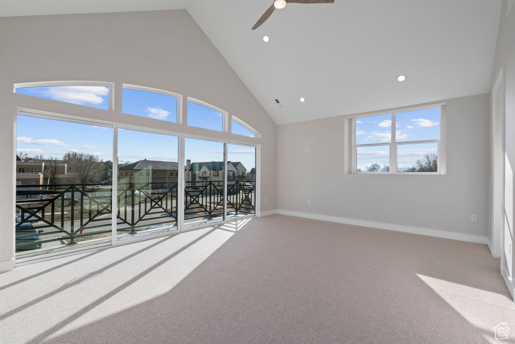Carpeted spare room featuring a wealth of natural light, ceiling fan, and high vaulted ceiling