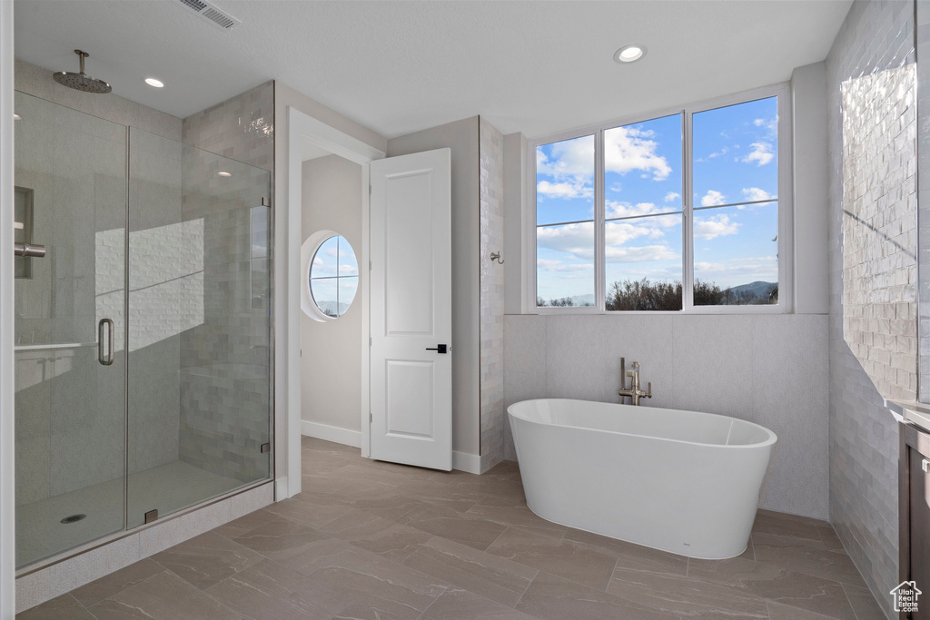 Bathroom with shower with separate bathtub, plenty of natural light, tile floors, and tile walls