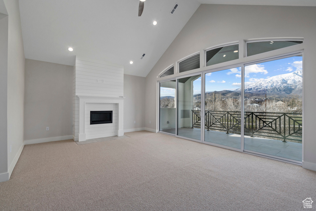 Unfurnished living room with light colored carpet, a mountain view, ceiling fan, high vaulted ceiling, and a large fireplace