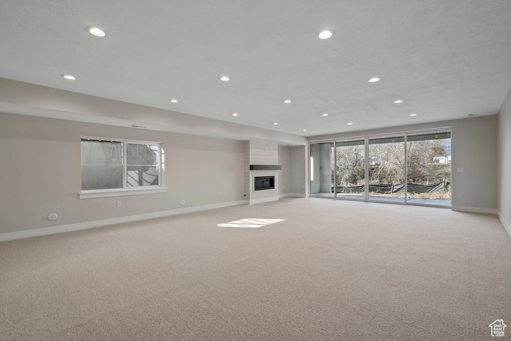 Unfurnished living room featuring a large fireplace and light colored carpet