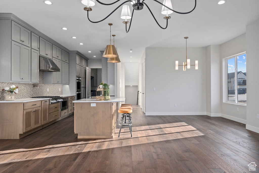 Kitchen featuring backsplash, dark wood-type flooring, hanging light fixtures, a kitchen island, and a kitchen bar