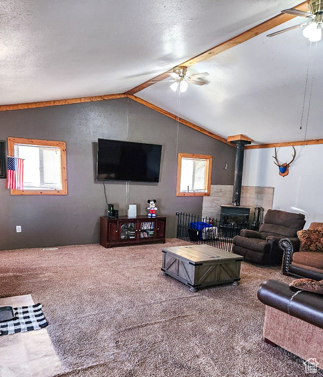 Carpeted living room featuring a textured ceiling, a wood stove, vaulted ceiling, and ceiling fan