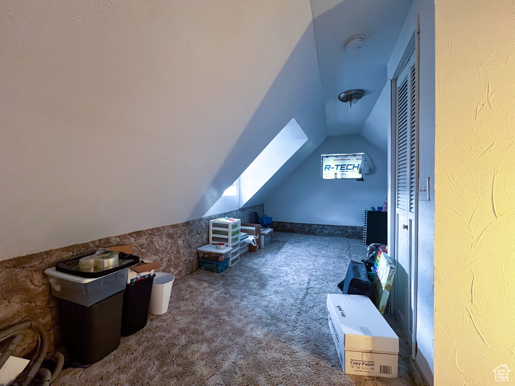 Additional living space with vaulted ceiling with skylight and dark colored carpet