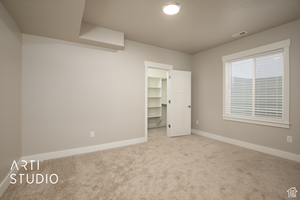 Unfurnished bedroom with a walk in closet, a closet, and light colored carpet