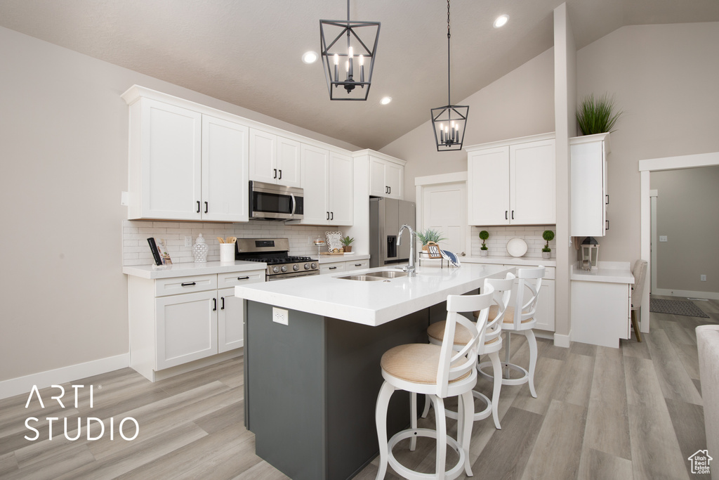 Kitchen featuring appliances with stainless steel finishes, pendant lighting, tasteful backsplash, light wood-type flooring, and white cabinetry