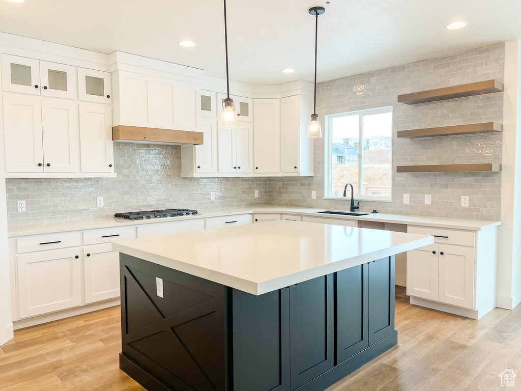 Kitchen featuring tasteful backsplash, white cabinetry, sink, light hardwood / wood-style flooring, and decorative light fixtures