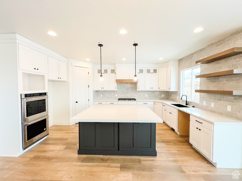 Kitchen with a kitchen island, sink, light hardwood / wood-style flooring, backsplash, and white cabinets