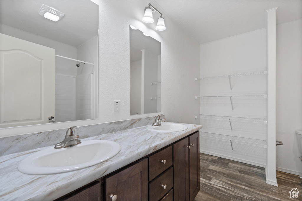 Bathroom featuring double sink, toilet, vanity with extensive cabinet space, and hardwood / wood-style flooring