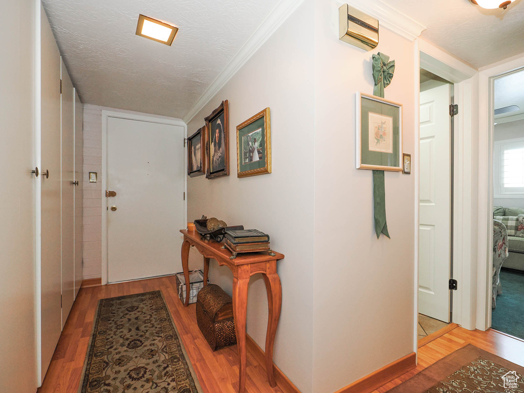 Hallway with a wall mounted air conditioner, hardwood / wood-style floors, a textured ceiling, and crown molding