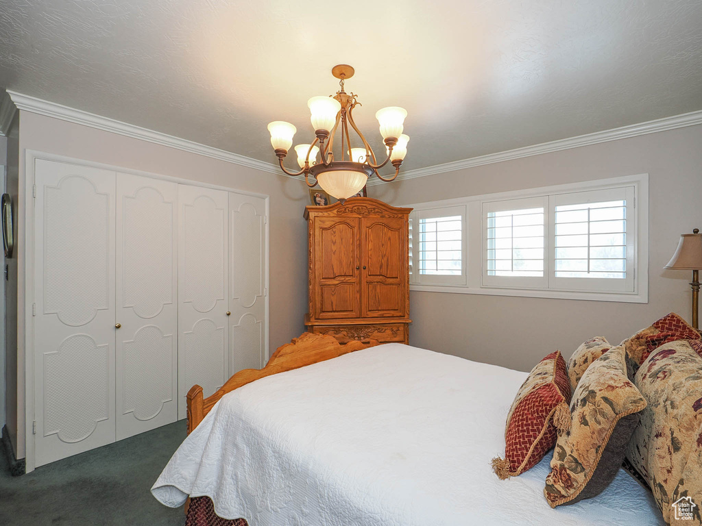 Bedroom featuring dark colored carpet, a closet, crown molding, and a notable chandelier