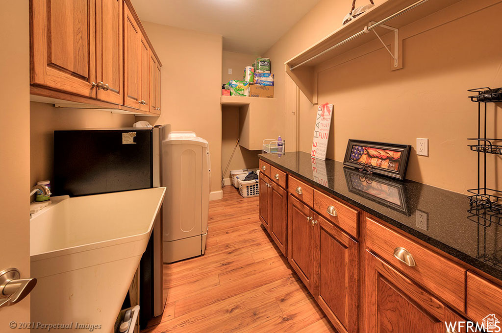 Laundry area featuring sink, light hardwood / wood-style flooring, washing machine and clothes dryer, and cabinets