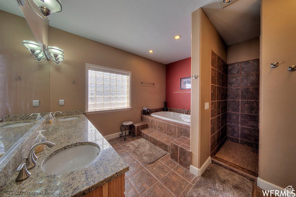 Bathroom with double vanity, an inviting chandelier, a relaxing tiled bath, and tile floors
