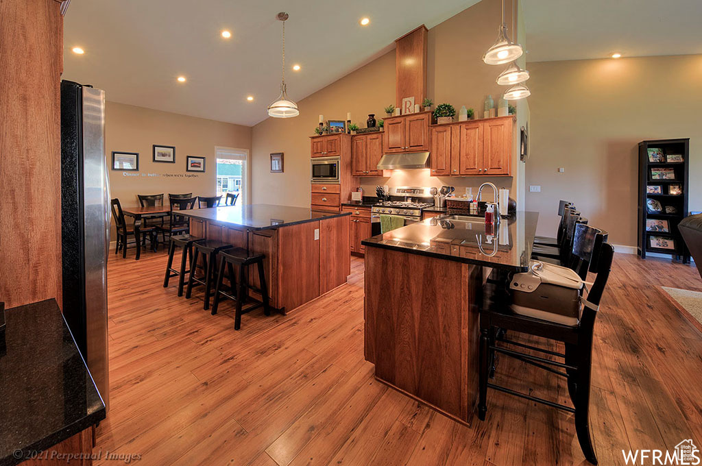 Kitchen with a kitchen breakfast bar, stainless steel appliances, sink, light wood-type flooring, and a center island