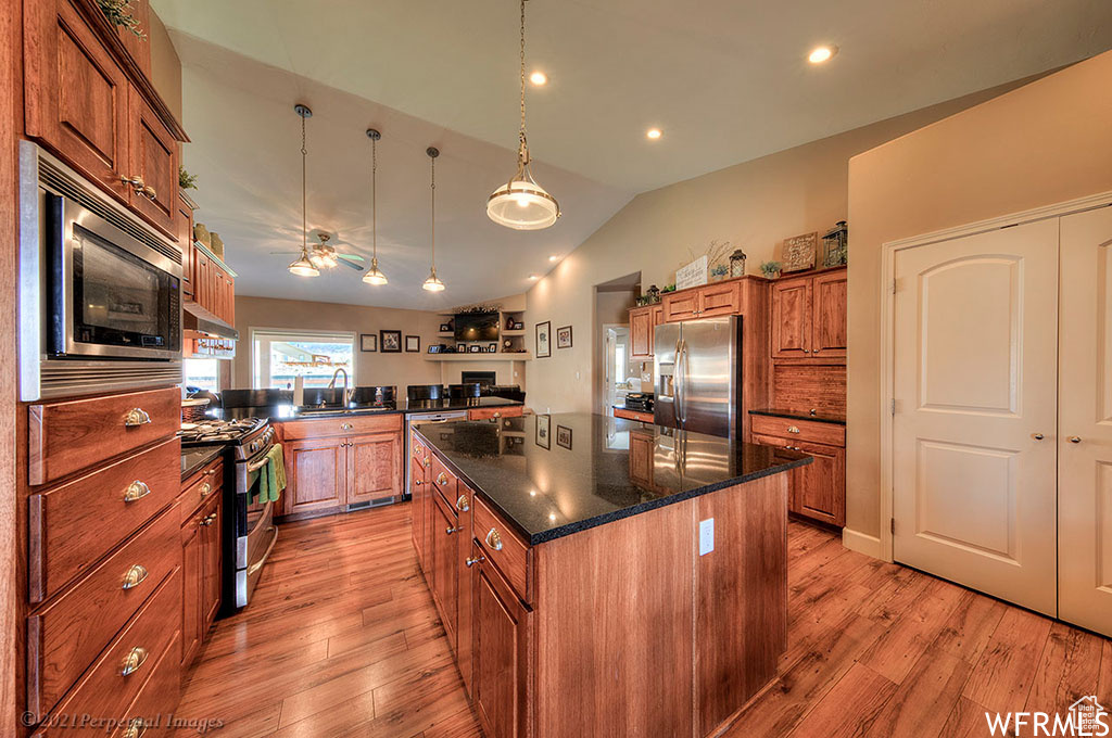 Kitchen featuring dark stone countertops, a center island, light hardwood / wood-style floors, hanging light fixtures, and stainless steel appliances