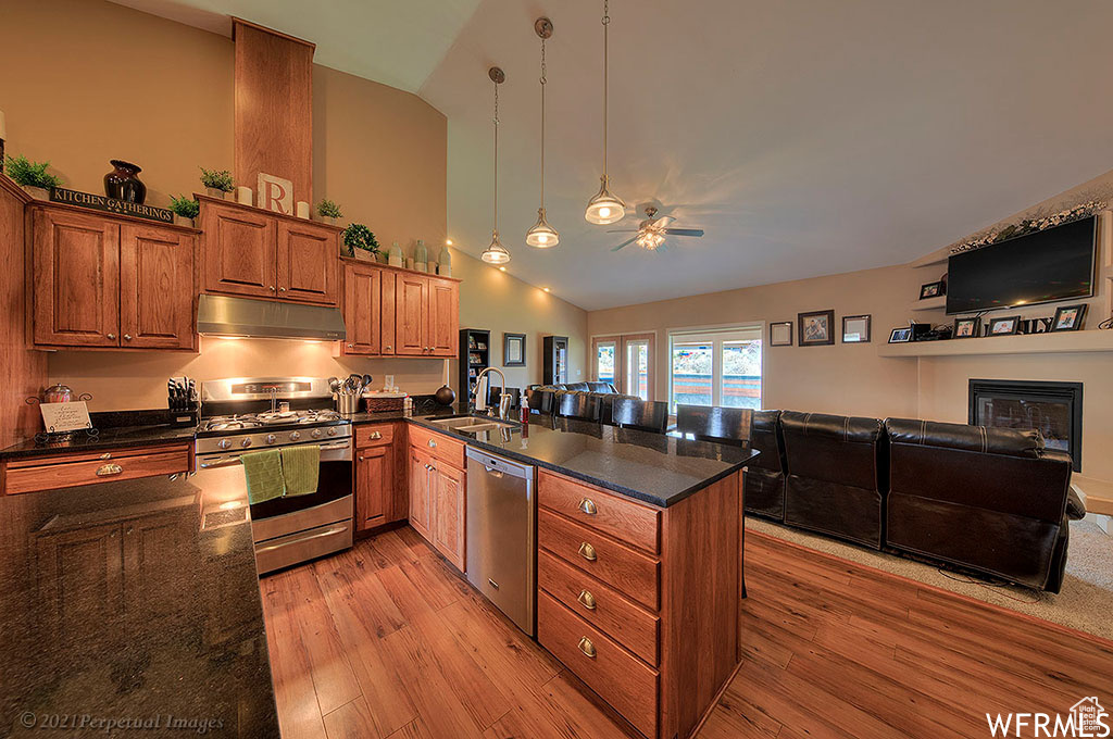 Kitchen with sink, appliances with stainless steel finishes, light hardwood / wood-style floors, pendant lighting, and dark stone counters