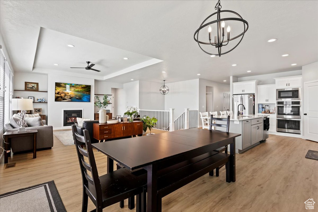 Dining area featuring a tray ceiling, sink, ceiling fan with notable chandelier, and light hardwood / wood-style floors