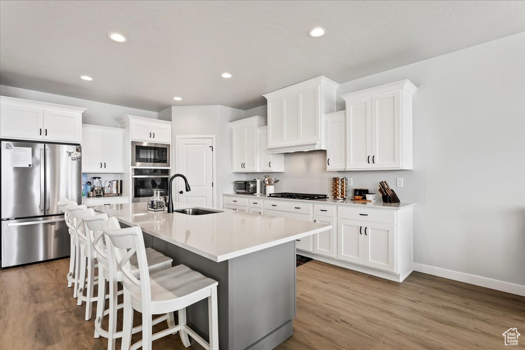 Kitchen featuring appliances with stainless steel finishes, a center island with sink, light hardwood / wood-style floors, and white cabinetry