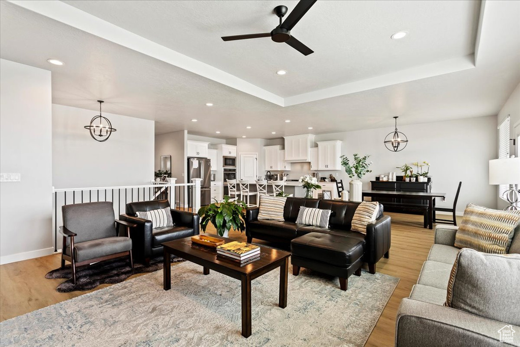 Living room with a raised ceiling, ceiling fan with notable chandelier, and light hardwood / wood-style flooring