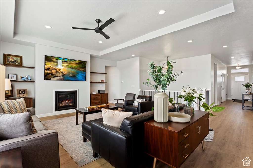 Living room featuring a raised ceiling, light wood-type flooring, and ceiling fan