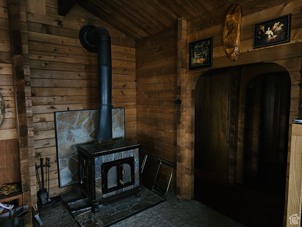 Unfurnished living room with wooden walls, vaulted ceiling, and a wood stove