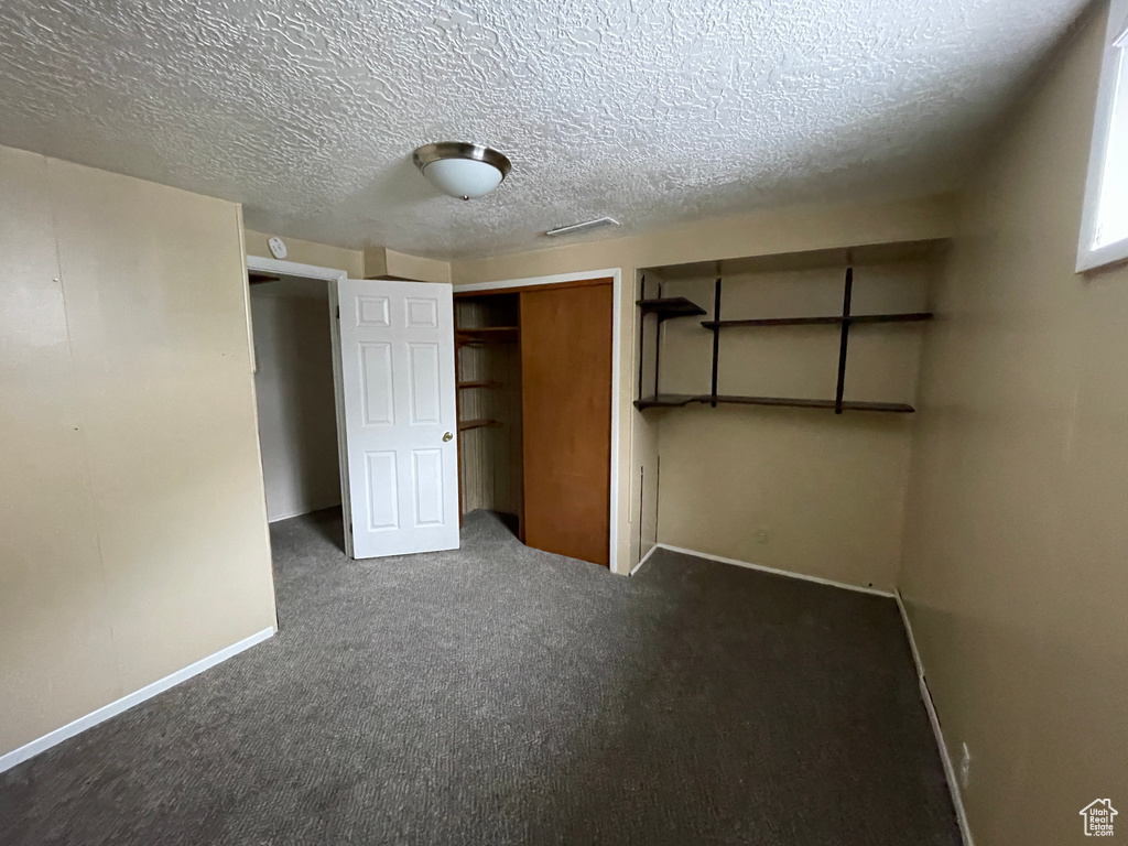 Unfurnished bedroom featuring a closet, a textured ceiling, and dark colored carpet