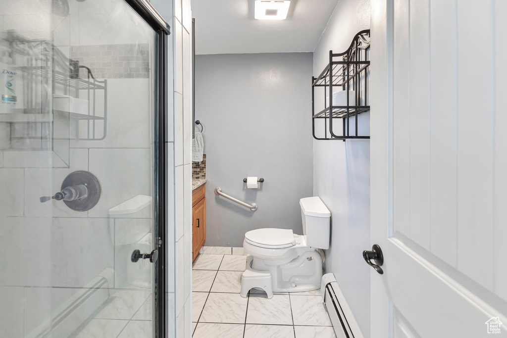 Bathroom featuring a shower with door, a baseboard heating unit, toilet, tile flooring, and vanity