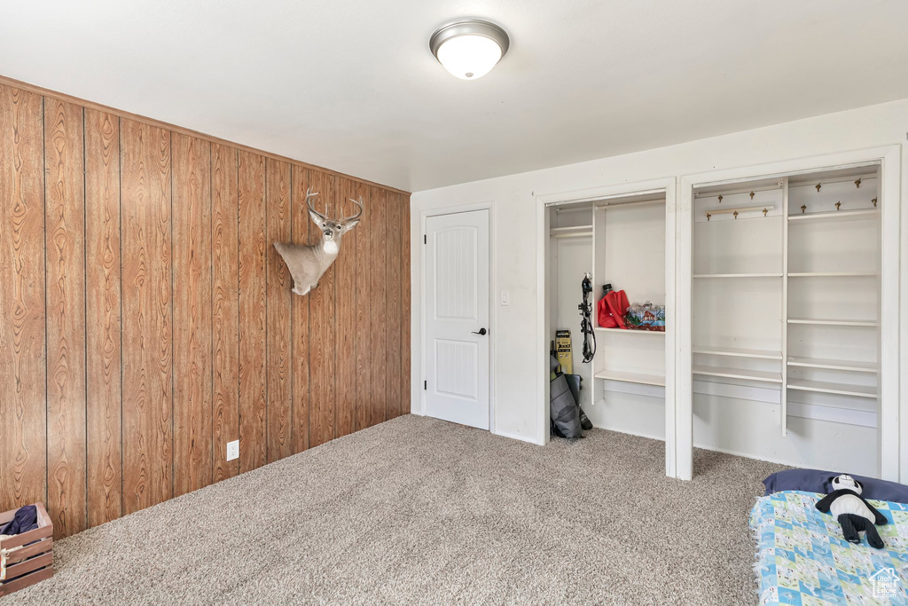Unfurnished bedroom with light colored carpet, wooden walls, and two closets