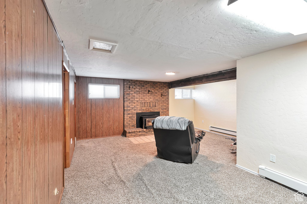 Basement with a textured ceiling, a baseboard heating unit, wooden walls, and a fireplace