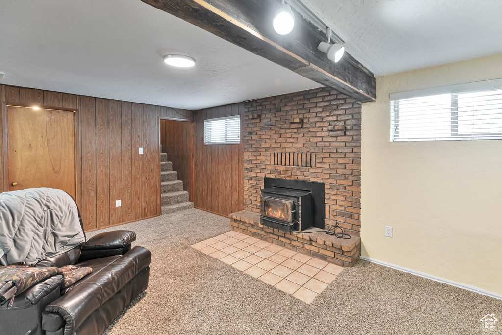 Carpeted living room featuring wooden walls, beam ceiling, a wood stove, brick wall, and a fireplace