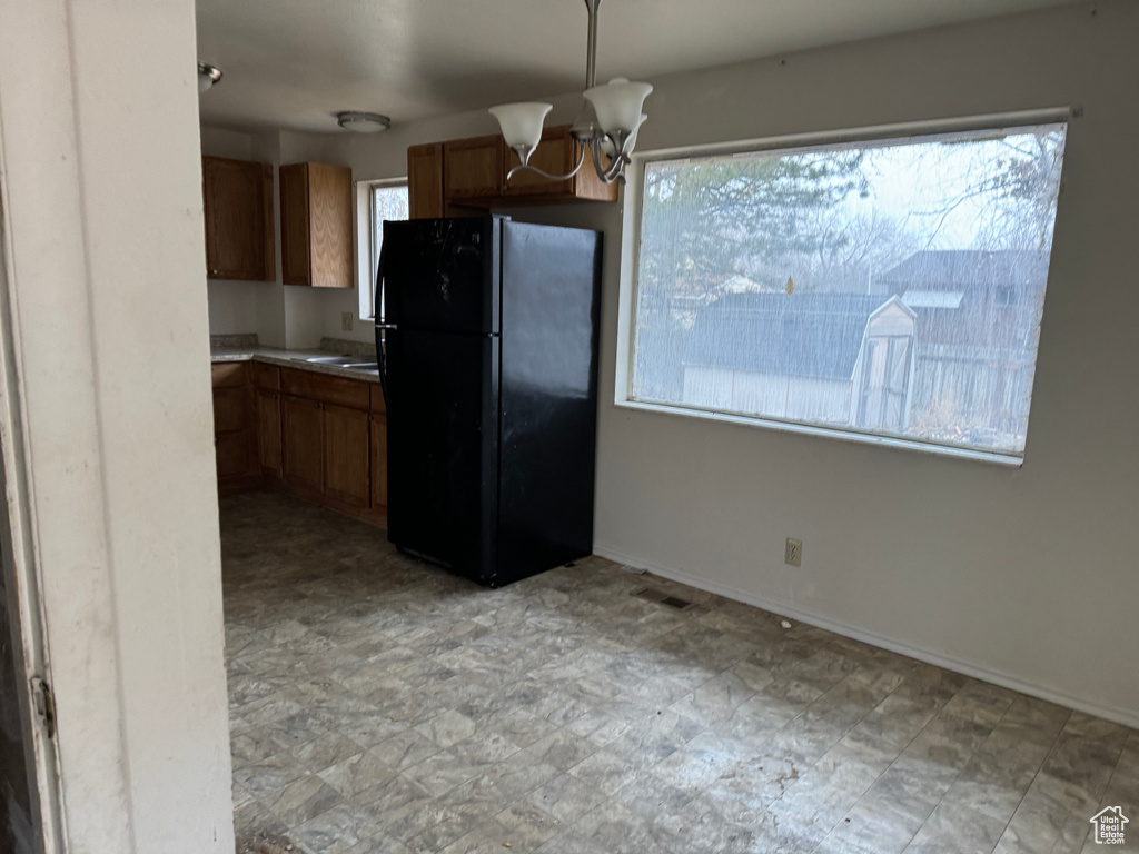 Kitchen with a healthy amount of sunlight, black fridge, a chandelier, and light tile floors